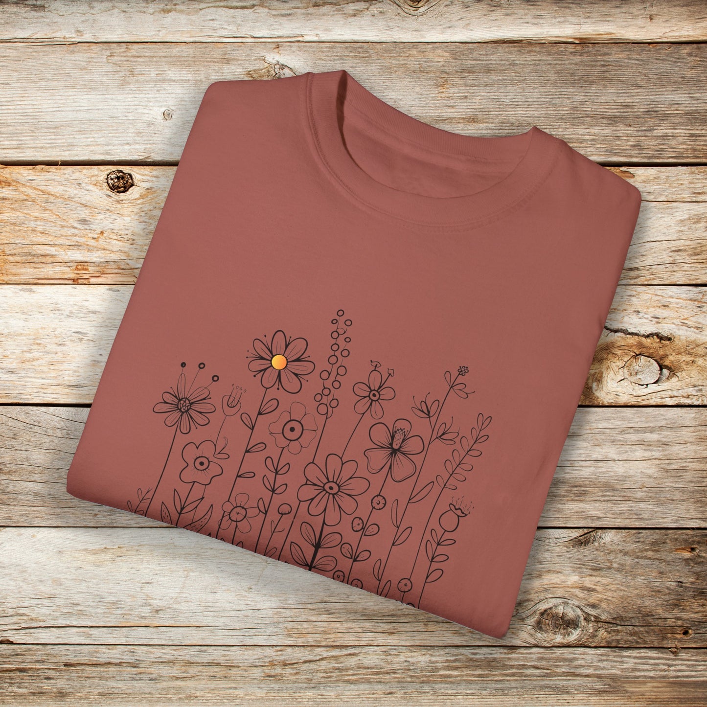 Cinnamon colored shirt with a minimalist black line art design featuring a variety of whimsical flowers and stems. One flower stands out with a small pop of yellow at its center, adding a subtle touch of color to the elegant floral arrangement.