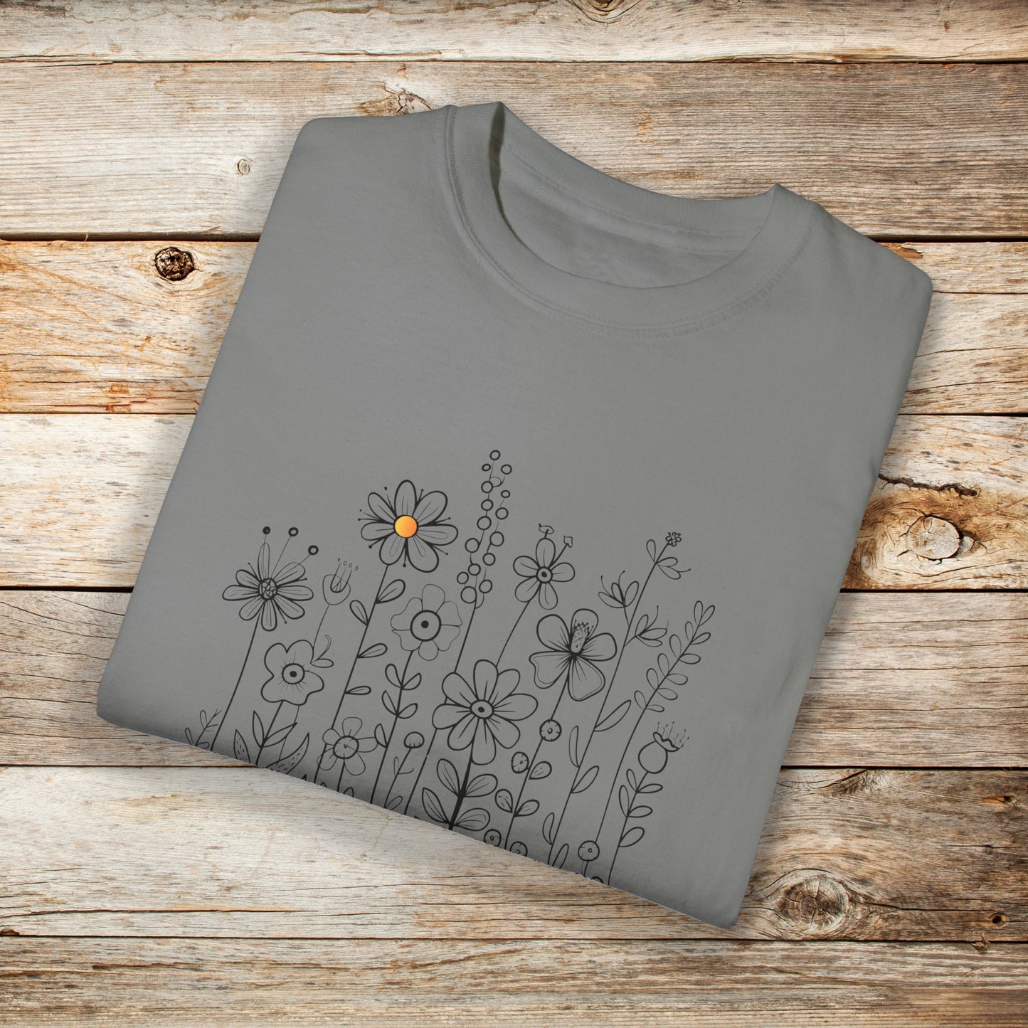 Light gray t-shirt with a minimalist black line art design featuring a variety of whimsical flowers and stems. One flower stands out with a small pop of yellow at its center, adding a subtle touch of color to the elegant floral arrangement.