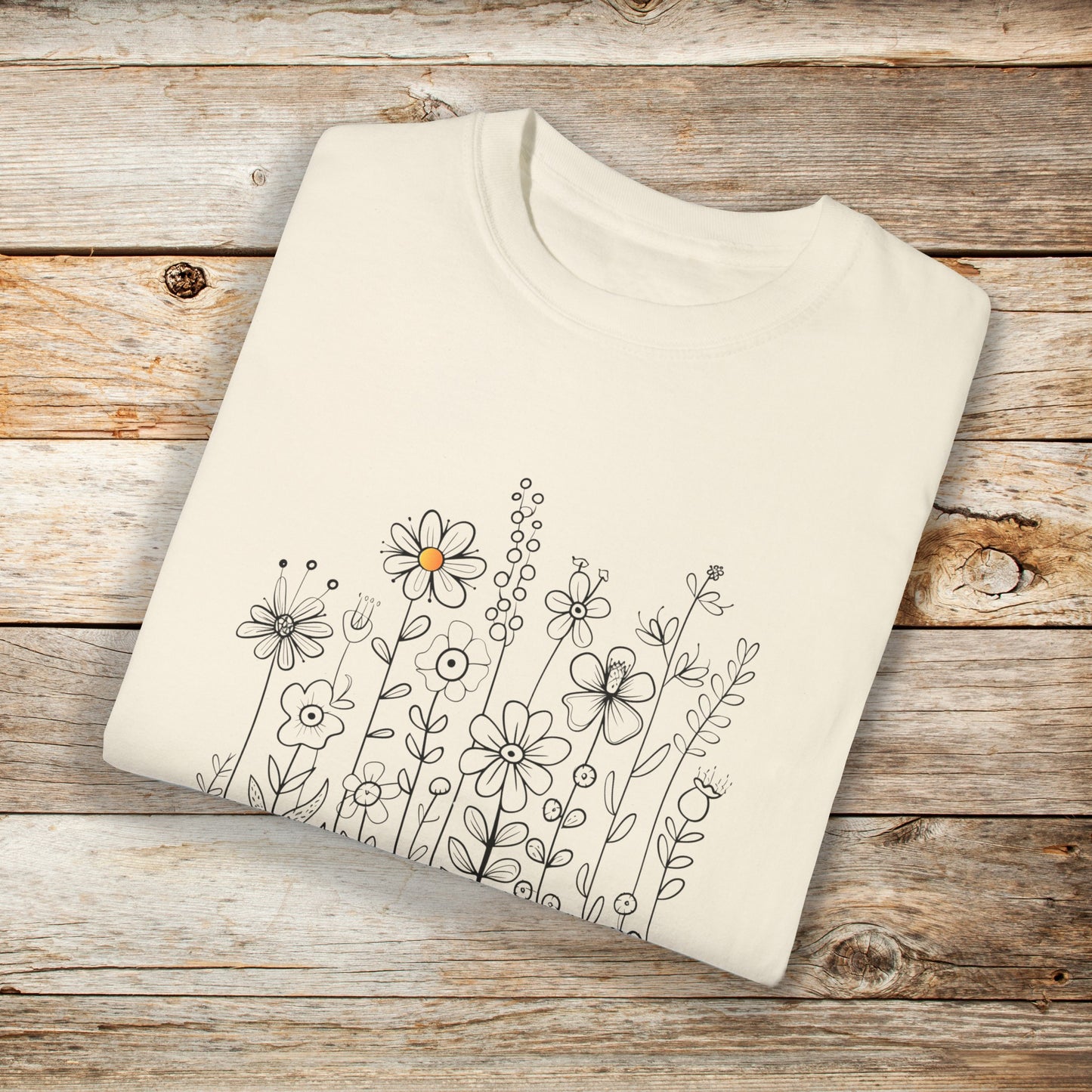 Ivory t-shirt with a minimalist black line art design featuring a variety of whimsical flowers and stems. One flower stands out with a small pop of yellow at its center, adding a subtle touch of color to the elegant floral arrangement
