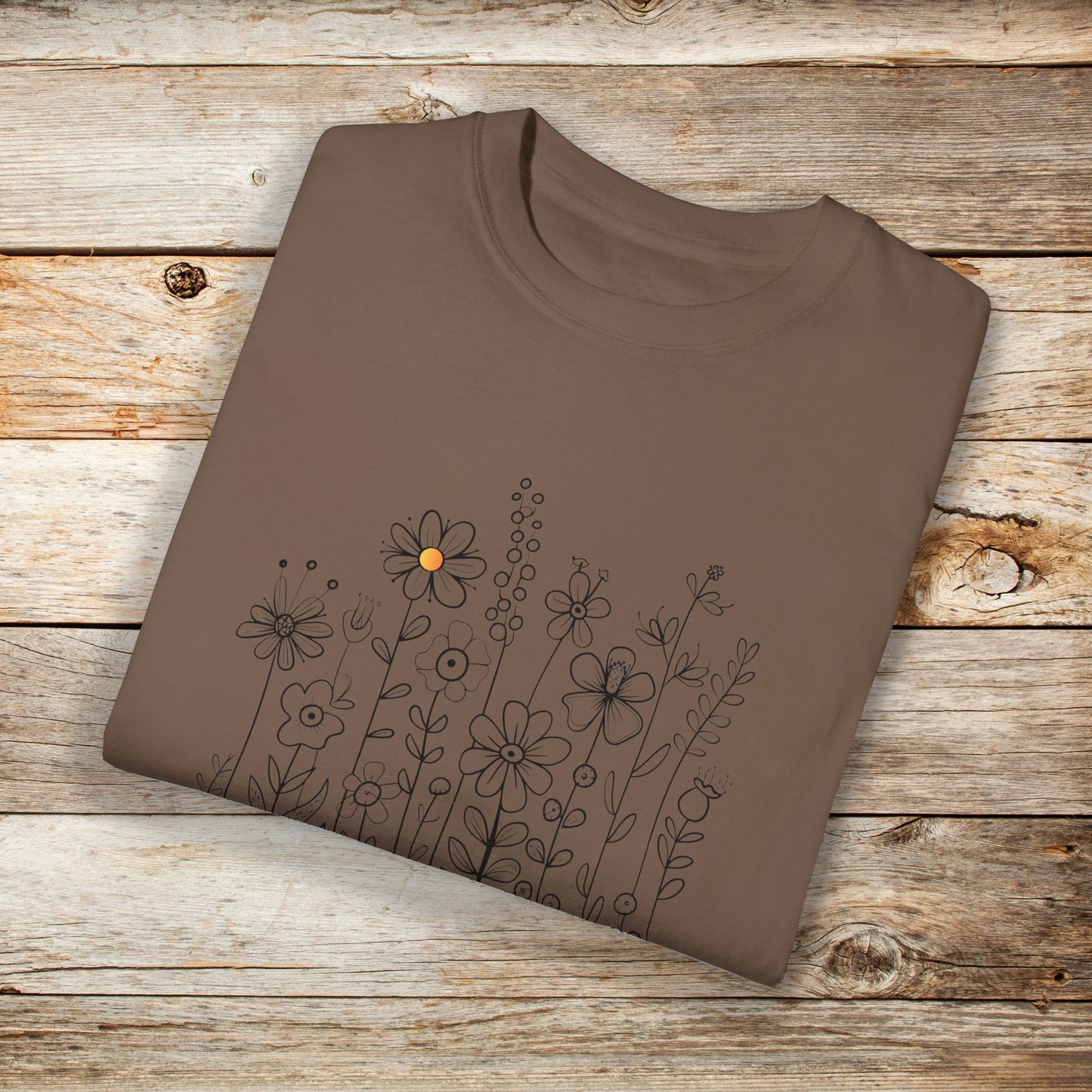 Espresso colored t-shirt with a minimalist black line art design featuring a variety of whimsical flowers and stems. One flower stands out with a small pop of yellow at its center, adding a subtle touch of color to the elegant floral arrangement.
