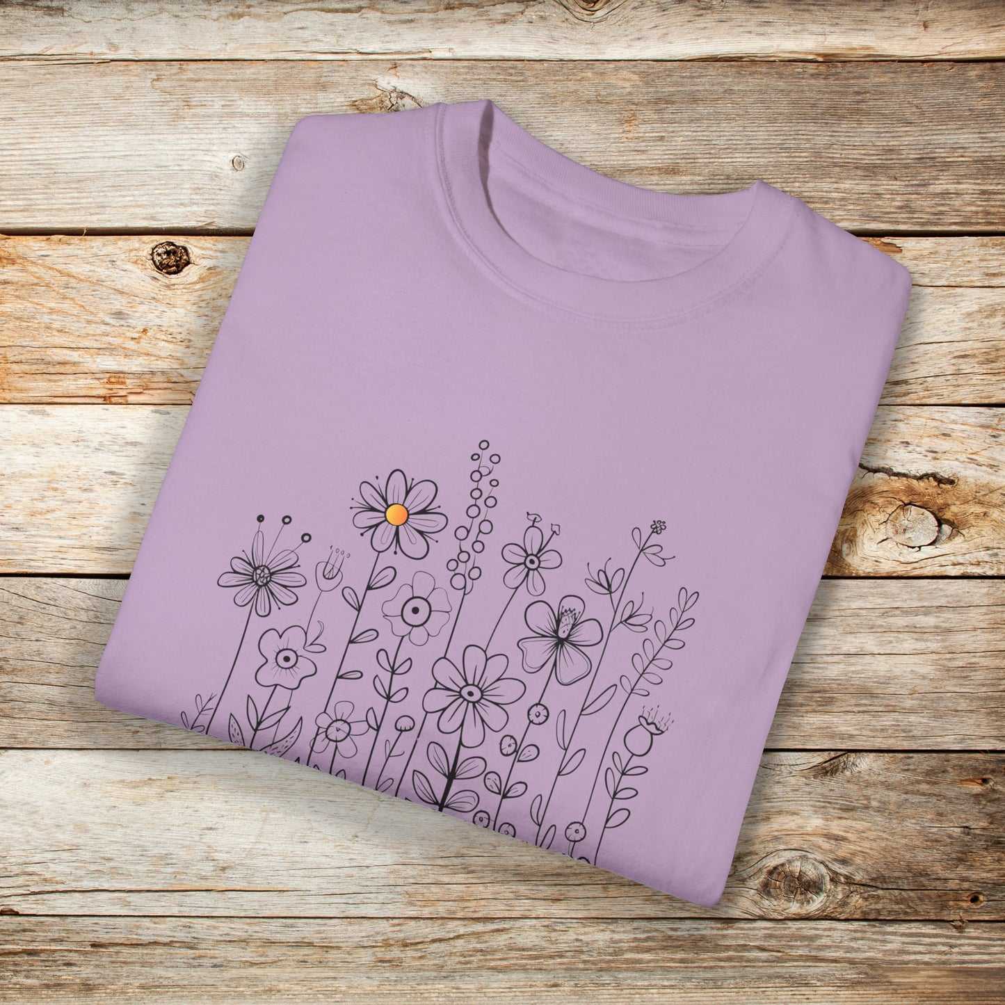 Violet t-shirt with a minimalist black line art design featuring a variety of whimsical flowers and stems. One flower stands out with a small pop of yellow at its center, adding a subtle touch of color to the elegant floral arrangement.