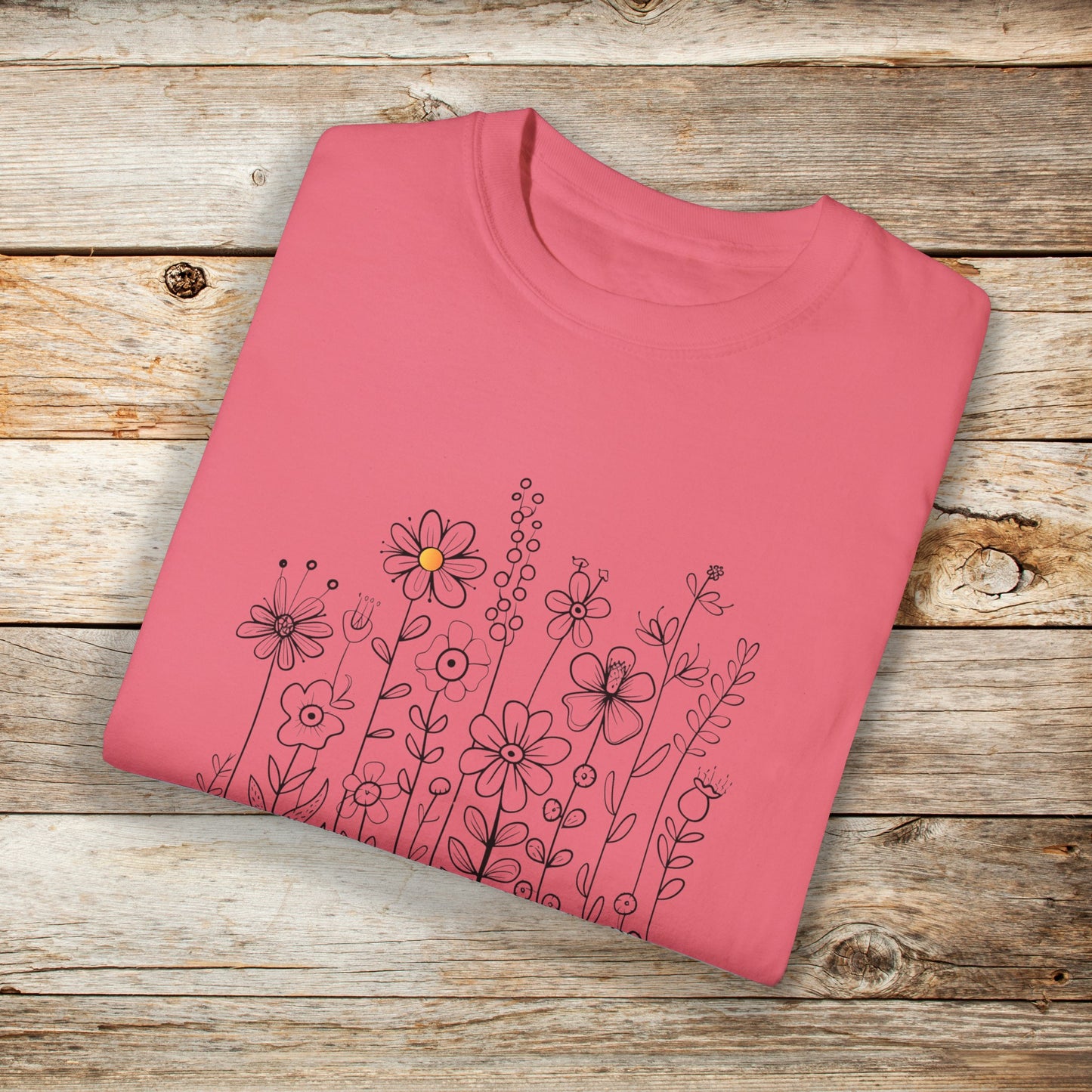 Watermelon pink shirt with a minimalist black line art design featuring a variety of whimsical flowers and stems. One flower stands out with a small pop of yellow at its center, adding a subtle touch of color to the elegant floral arrangement.