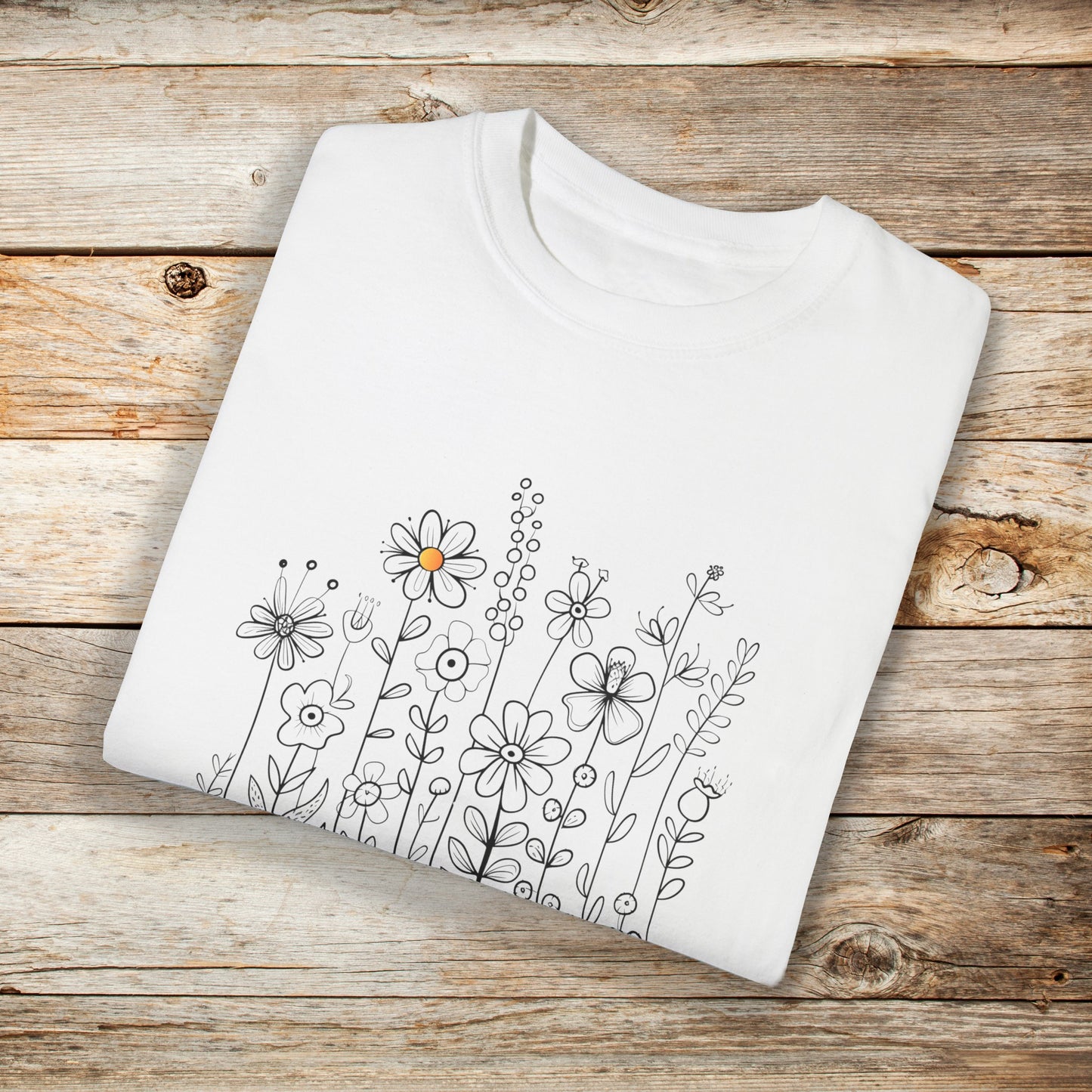 White t-shirt with a minimalist black line art design featuring a variety of whimsical flowers and stems. One flower stands out with a small pop of yellow at its center, adding a subtle touch of color to the elegant floral arrangement.