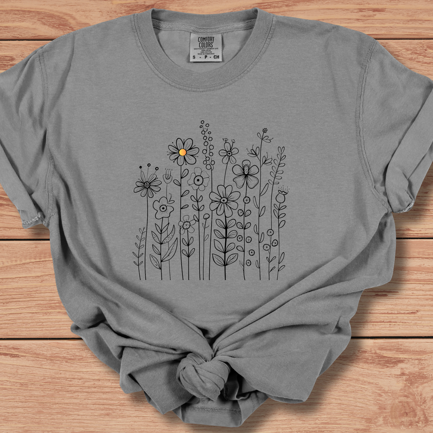 Light gray t-shirt with a minimalist black line art design featuring a variety of whimsical flowers and stems. One flower stands out with a small pop of yellow at its center, adding a subtle touch of color to the elegant floral arrangement.