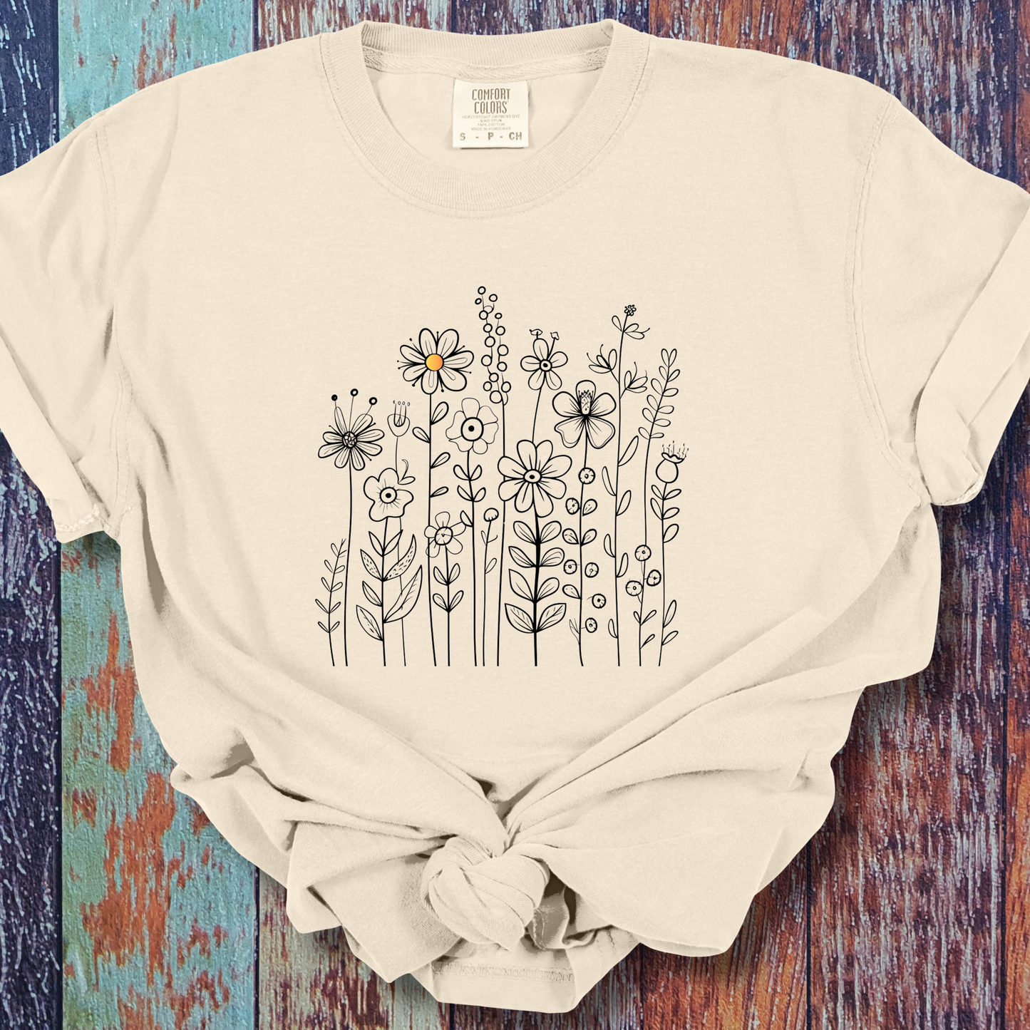 Ivory t-shirt with a minimalist black line art design featuring a variety of whimsical flowers and stems. One flower stands out with a small pop of yellow at its center, adding a subtle touch of color to the elegant floral arrangement