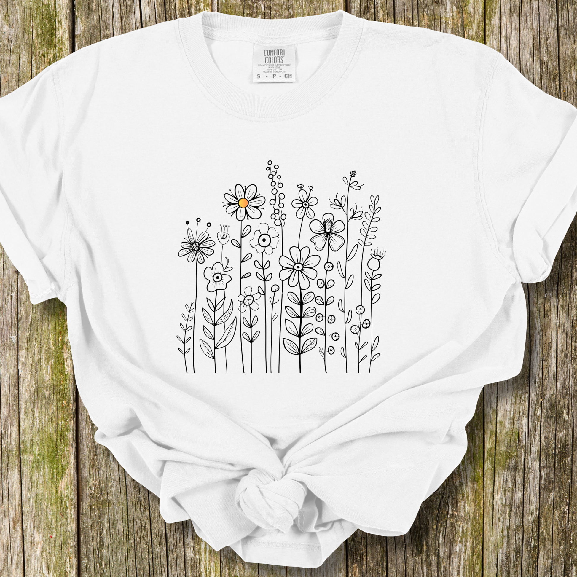 White t-shirt with a minimalist black line art design featuring a variety of whimsical flowers and stems. One flower stands out with a small pop of yellow at its center, adding a subtle touch of color to the elegant floral arrangement.