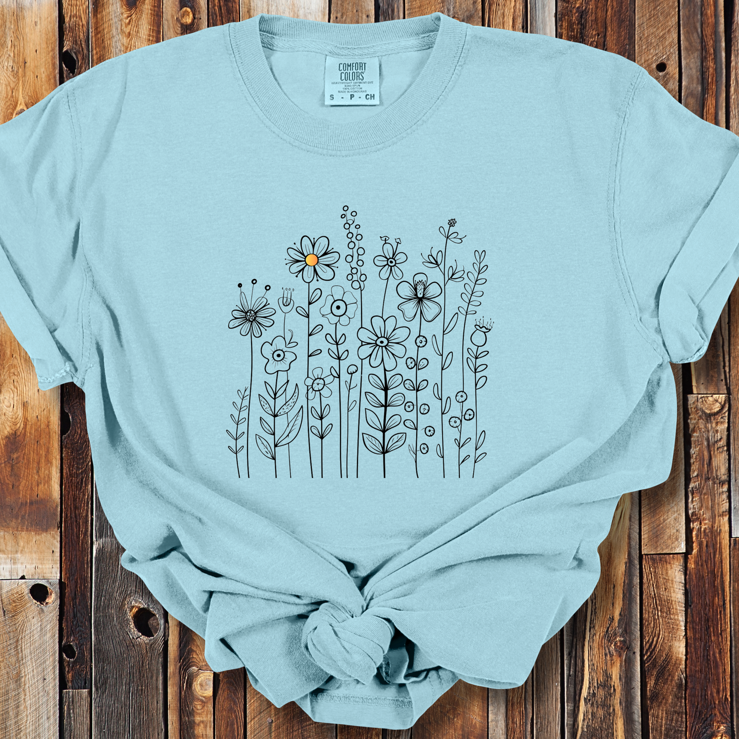 Chambray shirt with a minimalist black line art design featuring a variety of whimsical flowers and stems. One flower stands out with a small pop of yellow at its center, adding a subtle touch of color to the elegant floral arrangement.