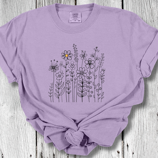 Violet t-shirt with a minimalist black line art design featuring a variety of whimsical flowers and stems. One flower stands out with a small pop of yellow at its center, adding a subtle touch of color to the elegant floral arrangement.